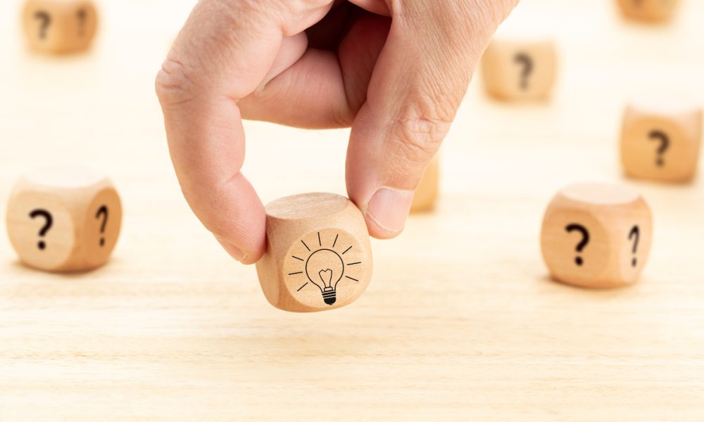 Creative idea or innovation concept. Hand picked wooden cube block with question mark symbol and light bulb icon on wood table